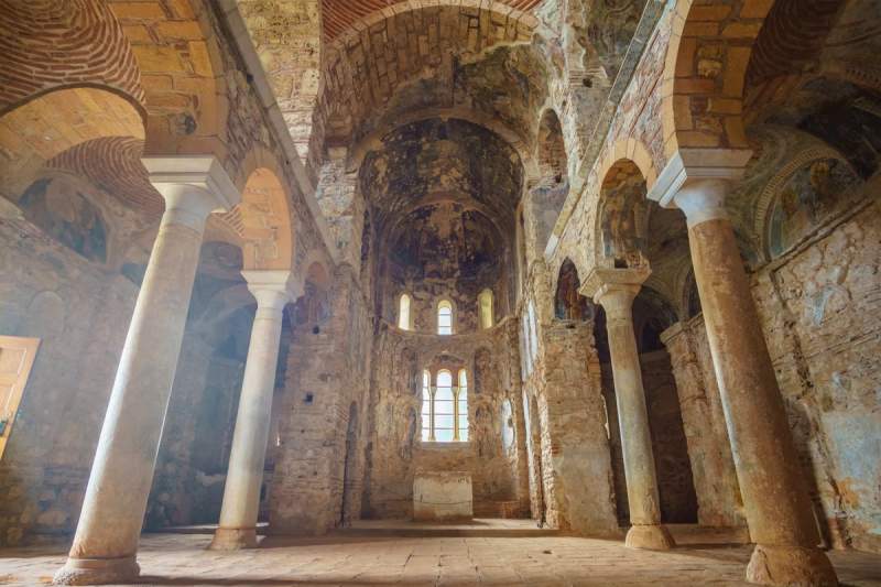 Intérieur d'une cathédrale byzantine à Mystra, avec des colonnes et des fresques anciennes.