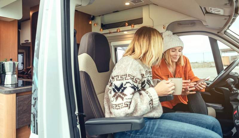 Deux femmes dans l'habitacle d'un camping-car consultant un smartphone, illustrant l'usage d'une eSIM en voyage itinérant