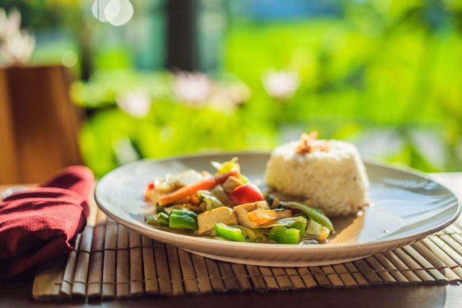 Assiette de légumes sautés avec du riz, un plat balinais servi dans un cadre naturel verdoyant.