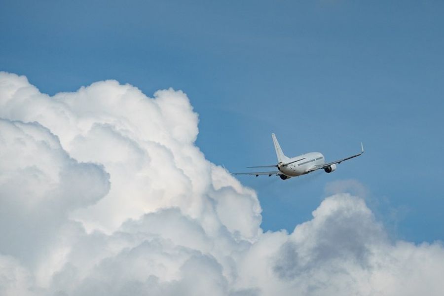 Un avion volant dans un ciel bleu avec de grands nuages blancs en arrière-plan.