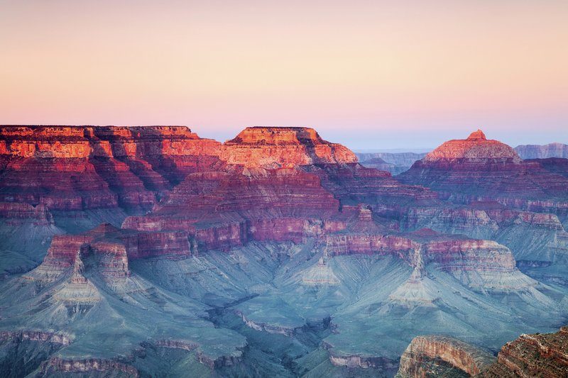 Coucher de soleil sur le Grand Canyon, falaises rocheuses baignées de lumière orangée contrastant avec les vallées bleutées en ombre