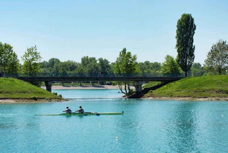 Vue paisible du lac Jarun avec des rameurs et un pont en arrière-plan, parfait pour des activités nautiques.