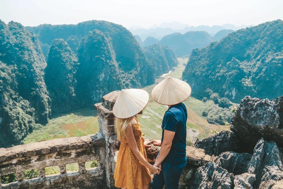 Couple en chapeaux coniques traditionnels admirant les pitons karstiques et rizières de Ninh Binh au Vietnam