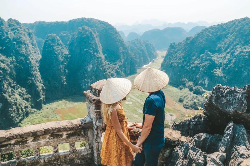 Couple en chapeaux coniques traditionnels admirant les pitons karstiques et rizières de Ninh Binh au Vietnam