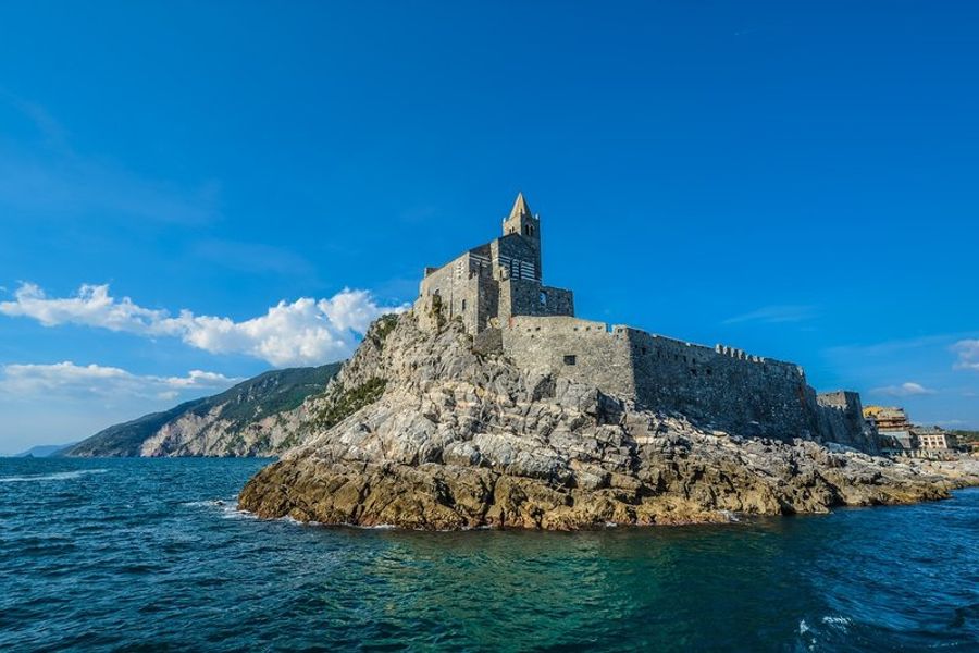 La majestueuse église de Portovenere perchée sur un rocher surplombant la mer, avec un ciel bleu clair en arrière-plan.