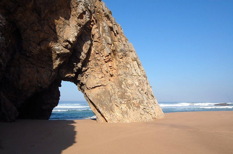 La plage sauvage de Praia da Adraga à Sintra, Portugal, caractérisée par ses falaises imposantes et son sable doré.