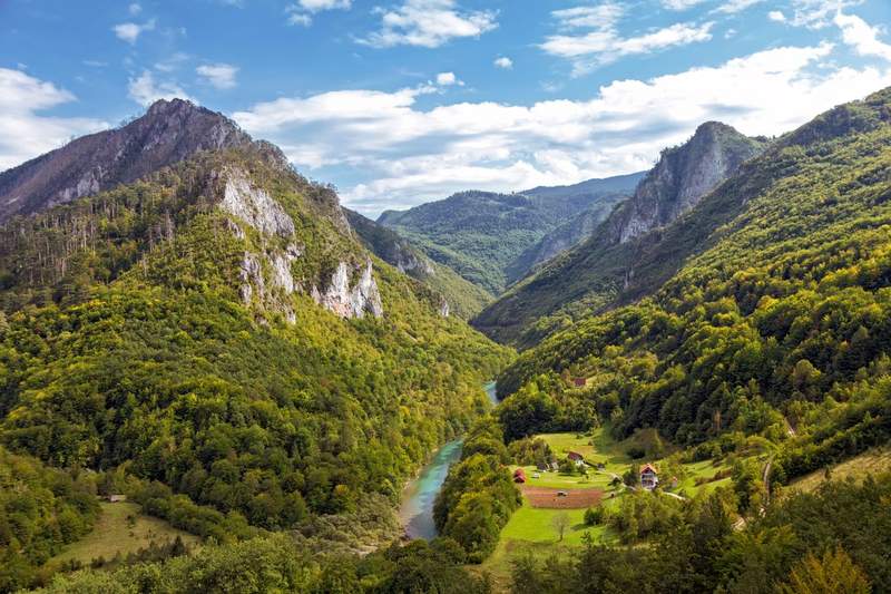 Vue panoramique sur la vallée de la rivière Tara dans le parc national du Durmitor au Monténégro, avec ses eaux turquoise serpentant entre des montagnes boisées et un hameau niché au fond du canyon