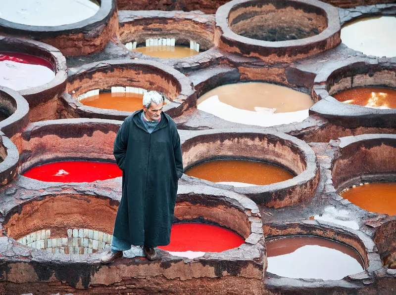 Tanneur marocain en djellaba devant les cuves colorées de la tannerie Chouara à Fès