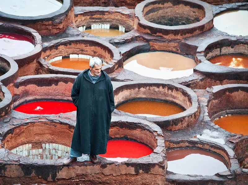 Tanneur marocain en djellaba devant les cuves colorées de la tannerie Chouara à Fès