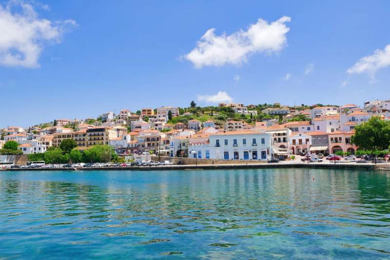 Vue panoramique de la ville côtière de Pylos, en Grèce, avec des bâtiments aux toits orange, bordant une mer calme sous un ciel bleu
