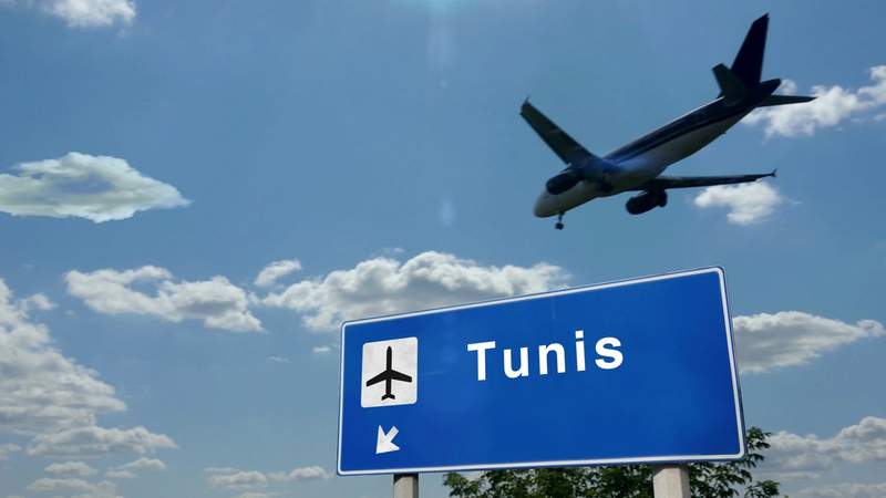 Panneau de signalisation indiquant l'aéroport de Tunis avec un avion en approche dans un ciel bleu
