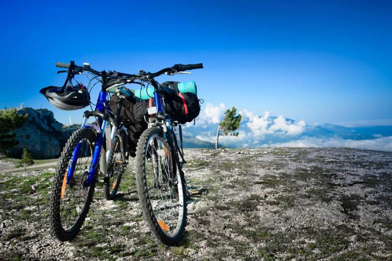 Deux vélos de randonnée chargés de sacoches posés sur un plateau rocheux avec vue sur les montagnes et les nuages.