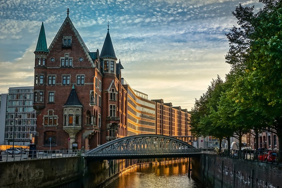Pont métallique sur un canal à Hambourg au coucher du soleil, avec des bâtiments historiques en briques et des arbres en bordure.