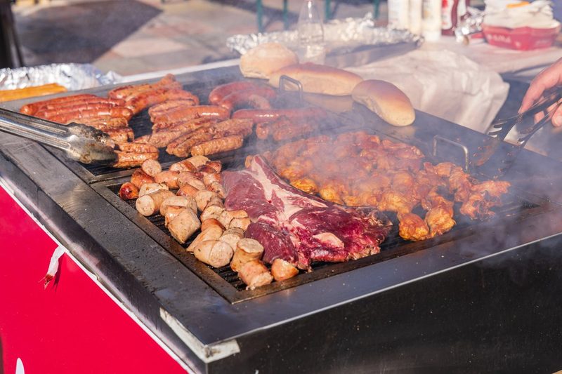 Barbecue extérieur à Tirana en Albanie avec saucisses grillées, brochettes, pièce de bœuf et morceaux de poulet marinés sur une grande plancha fumante