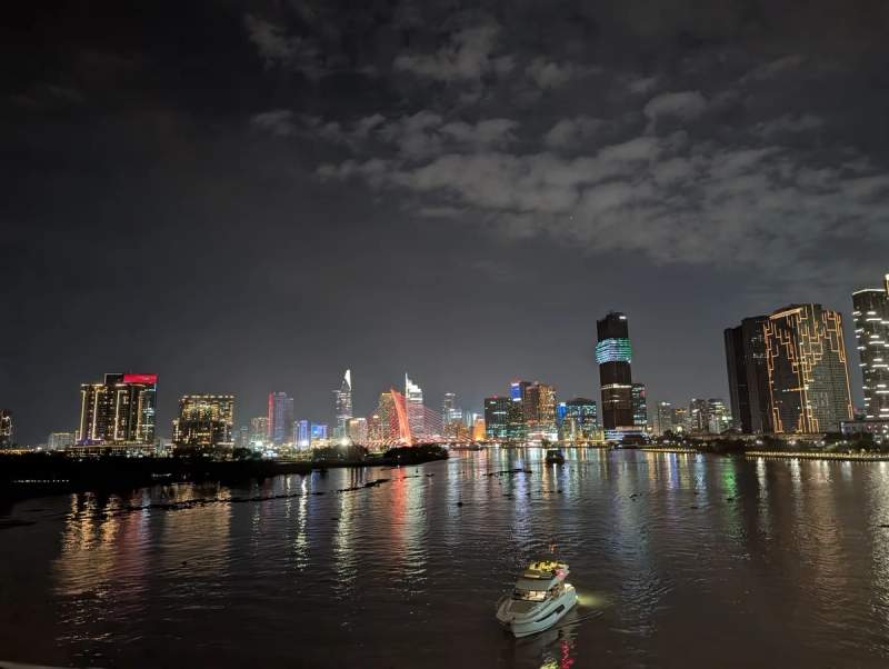 Vue nocturne de la rivière Saïgon avec les lumières des gratte-ciels et un bateau illuminé au premier plan