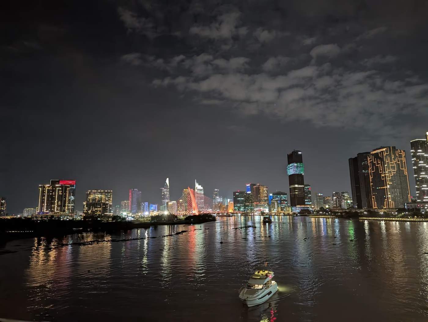Vue nocturne de la rivière Saïgon avec les lumières des gratte-ciels et un bateau illuminé au premier plan