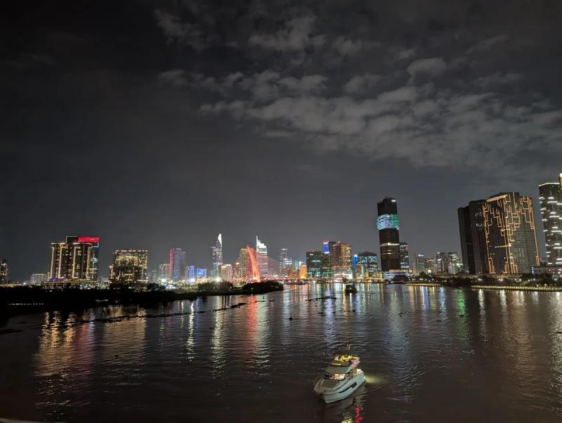 Vue nocturne de la rivière Saïgon avec les lumières des gratte-ciels et un bateau illuminé au premier plan