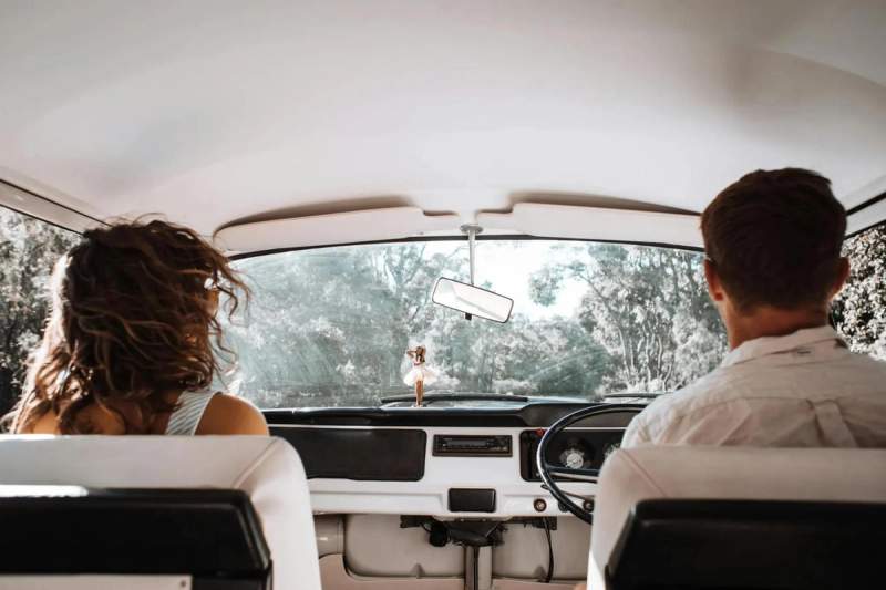 Couple en road trip, vue de l'intérieur de la voiture avec la route devant eux, symbolisant une aventure romantique et relaxante.