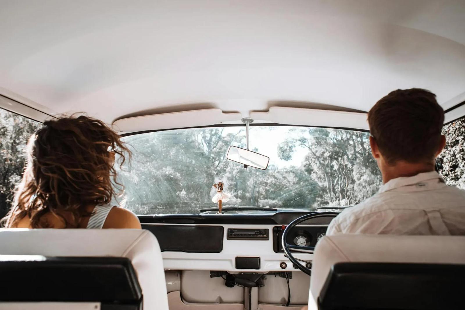 Couple en road trip, vue de l'intérieur de la voiture avec la route devant eux, symbolisant une aventure romantique et relaxante.