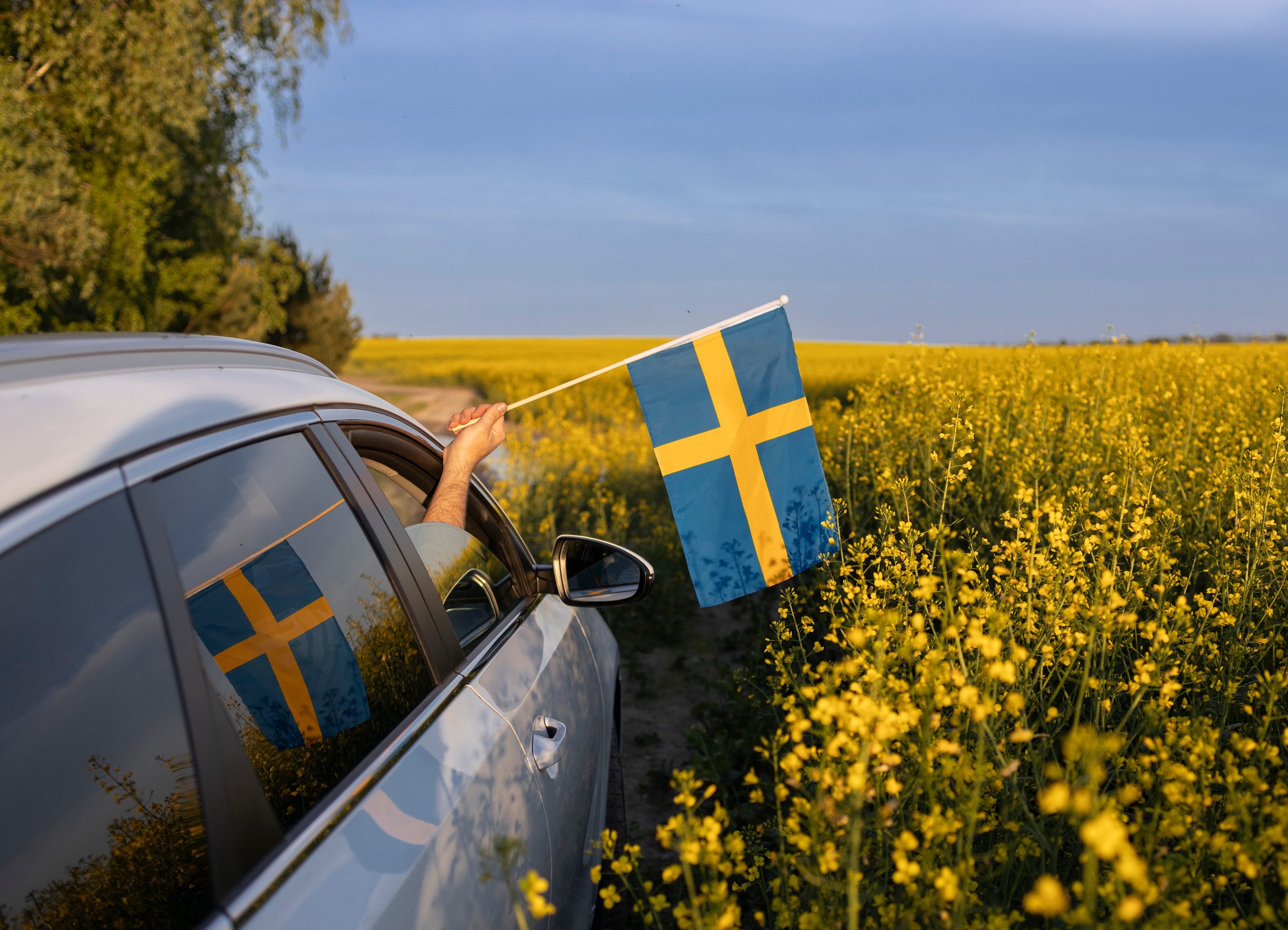 Voiture sur une route de campagne en Suède, avec un drapeau suédois à la fenêtre