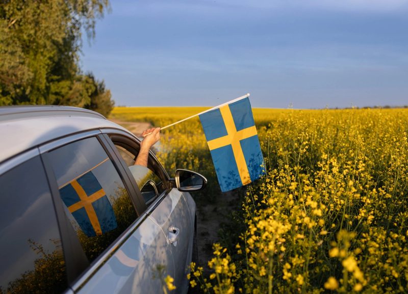 Voiture sur une route de campagne en Suède, avec un drapeau suédois à la fenêtre