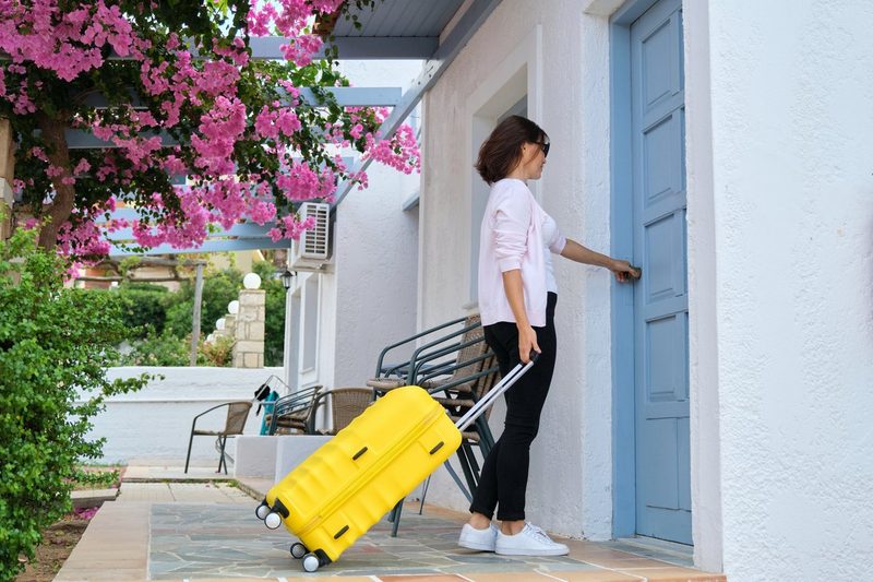 Femme avec valise jaune entrant dans un logement de location saisonnière pour financer ses voyages