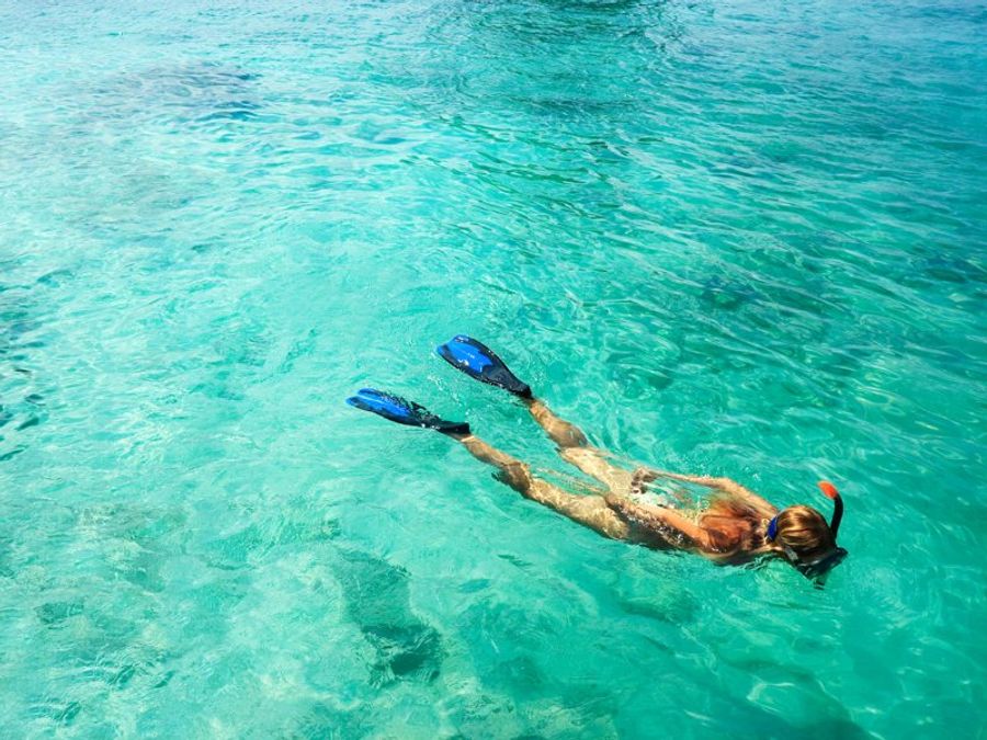 Personne pratiquant le snorkeling dans une mer turquoise limpide, équipée de palmes et tuba.