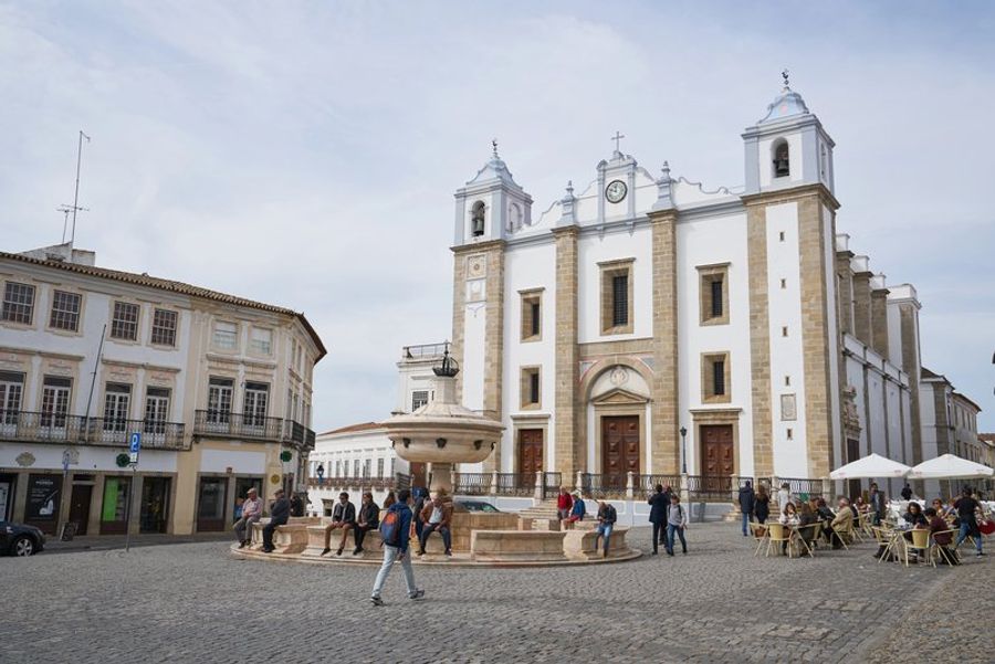 Vue animée de la Praça do Giraldo à Évora, entourée de bâtiments historiques et de cafés en plein air.