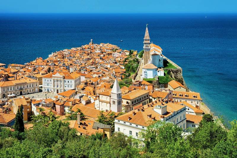Vue aérienne de Piran et sa presqu'île aux toits orangés entourée par la mer Adriatique, avec l'église Saint-Georges au sommet