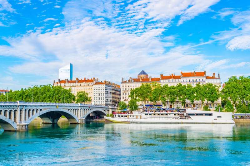 Vue panoramique du pont de Lyon sur le Rhône avec immeubles haussmanniens et bateau amarré sous un ciel bleu.