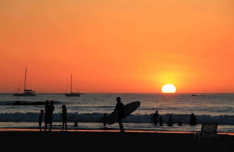 Coucher de soleil sur la plage de Tamarindo avec des silhouettes de surfeurs et de familles au bord de l'eau.