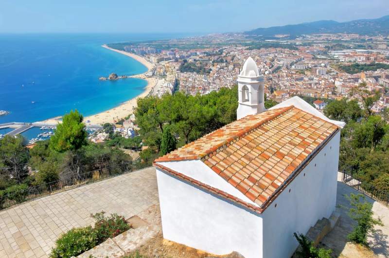 Vue aérienne sur la plage de Blanes, la ville et la mer Méditerranée, avec une chapelle blanche en premier plan.