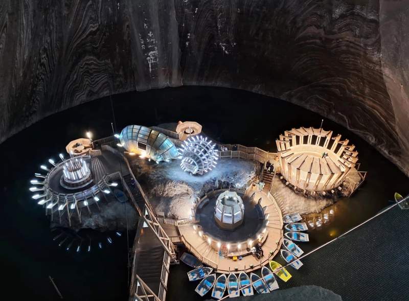 Vue aérienne de la mine de sel de Turda avec ses structures lumineuses et barques autour d'un lac souterrain.