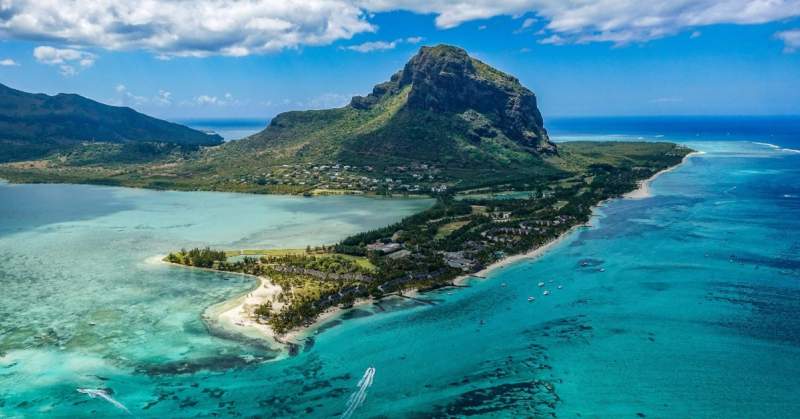 Vue aérienne spectaculaire de la montagne Le Morne à l’île Maurice, entourée de lagons turquoise et de plages de sable blanc.