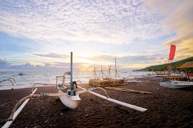 Bateau de pêche traditionnel balinais sur une plage de sable noir à Amed, au lever du soleil.