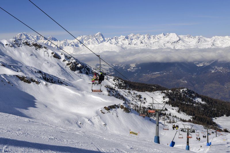 Pistes enneigées de la station de ski de Pila avec des skieurs sur les remontées mécaniques et une vue spectaculaire sur les Alpes.