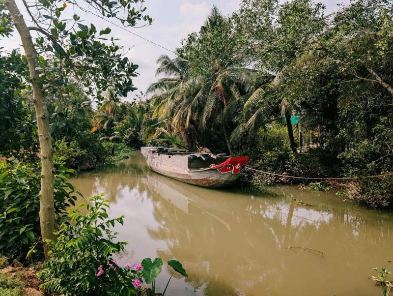 Bateau traditionnel amarré dans un canal entouré de végétation tropicale sur l’île d’An Binh à Vinh Long, dans le delta du Mékong.