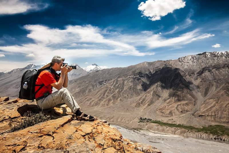 Voyageur photographiant un paysage montagneux depuis un sommet rocheux avec son appareil photo.