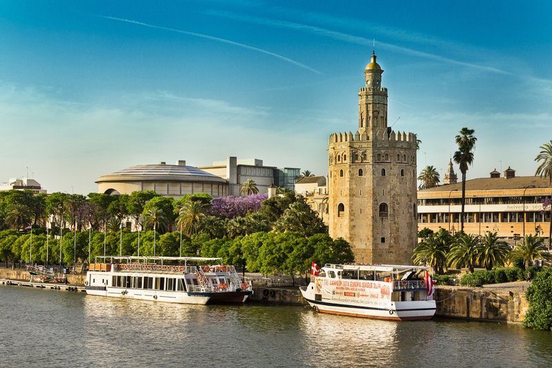 Vue de la Torre del Oro au bord du fleuve Guadalquivir, avec des bateaux amarrés prêts pour des visites touristiques.