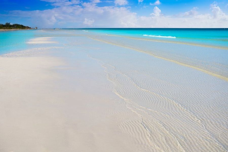 Plage de sable blanc immaculée à Holbox, baignée par une eau turquoise peu profonde sous un ciel ensoleillé.