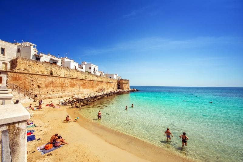 Une plage avec un mur historique et des baigneurs.