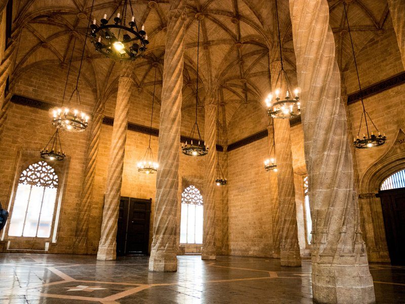 Intérieur de la Lonja de la Seda à Valence, Espagne, montrant de grandes colonnes torsadées sous des plafonds voûtés gothiques avec des lustres suspendus.