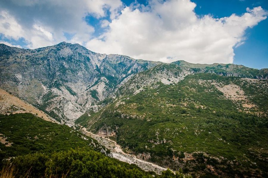 Vaste paysage montagneux avec des vallées verdoyantes et des collines sous un ciel partiellement nuageux.