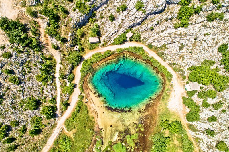 Vue aérienne de la source de la rivière Cetina avec des eaux turquoise entourées de végétation et de roches.