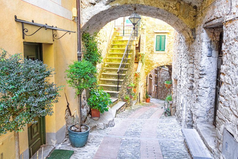 Charmante ruelle de la vieille ville de Dolceaqua, avec des arcades en pierre, des plantes en pot et des façades colorées.