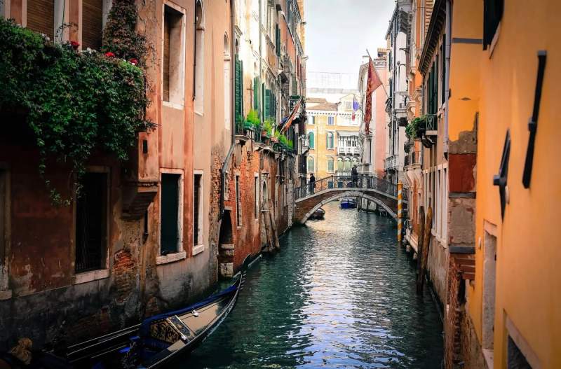 Un canal pittoresque à Venise, bordé de bâtiments historiques et colorés, avec une gondole amarrée et un pont charmant à l'horizon, capturant l'essence romantique de la ville.