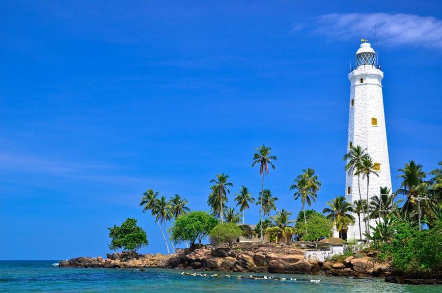 Le phare blanc de Dondra entouré de palmiers, sur la côte sud du Sri Lanka, sous un ciel bleu éclatant.