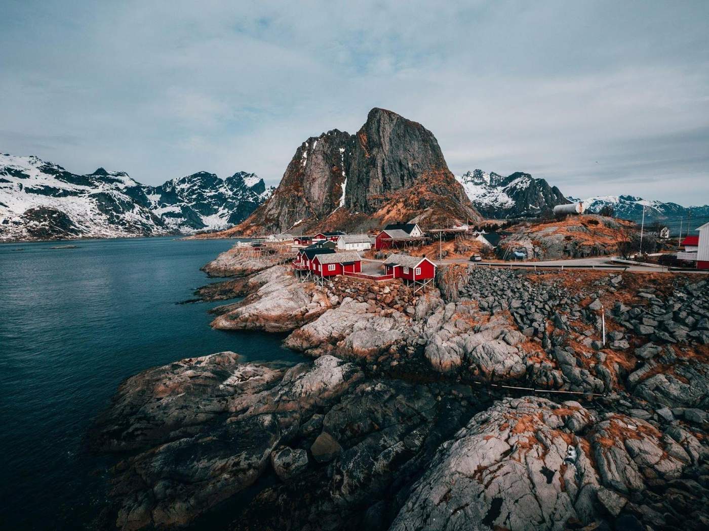 Vue pittoresque de maisons rouges sur une côte rocheuse avec des montagnes enneigées en arrière-plan en Norvège. 
