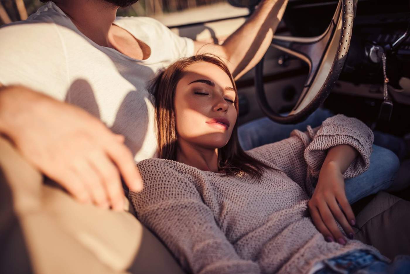 Jeune femme reposée, allongée contre son partenaire dans une voiture, symbolisant un moment paisible et complice pendant un road trip en amoureux.