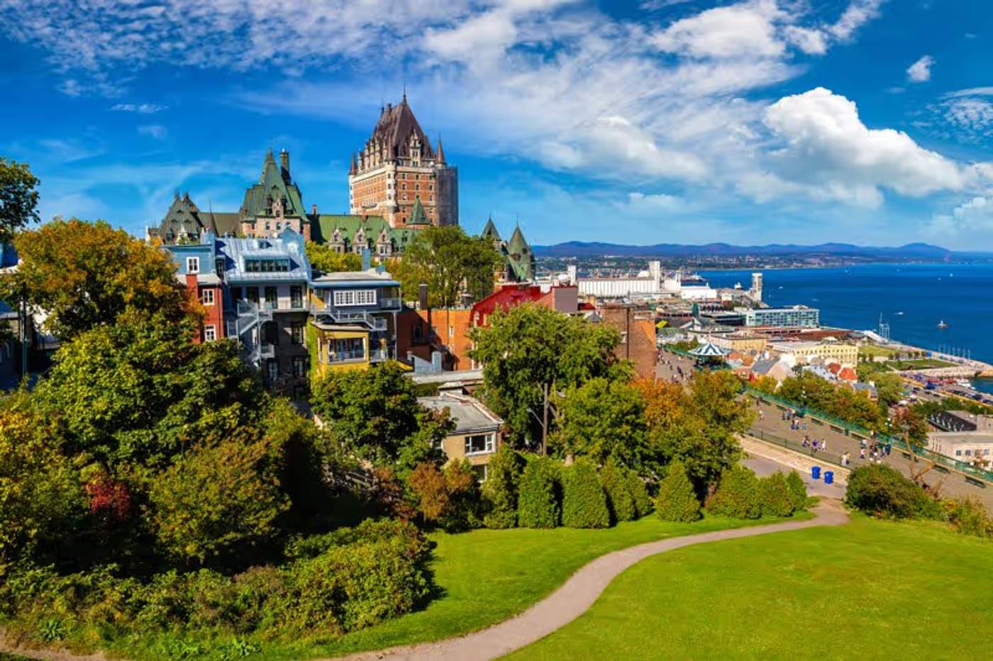 Vue sur le Château Frontenac dominant la ville de Québec, entouré d’arbres et de bâtiments colorés, avec le fleuve Saint-Laurent au fond.